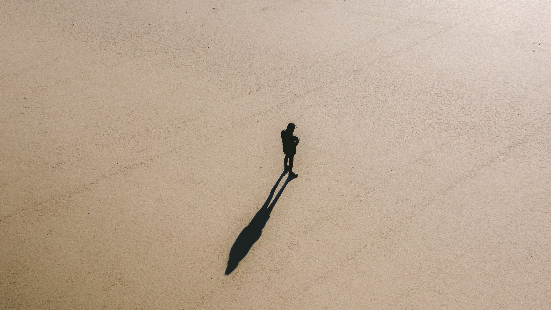 An aerial view of a lone figure and long shadow crossing a cracked salt flat